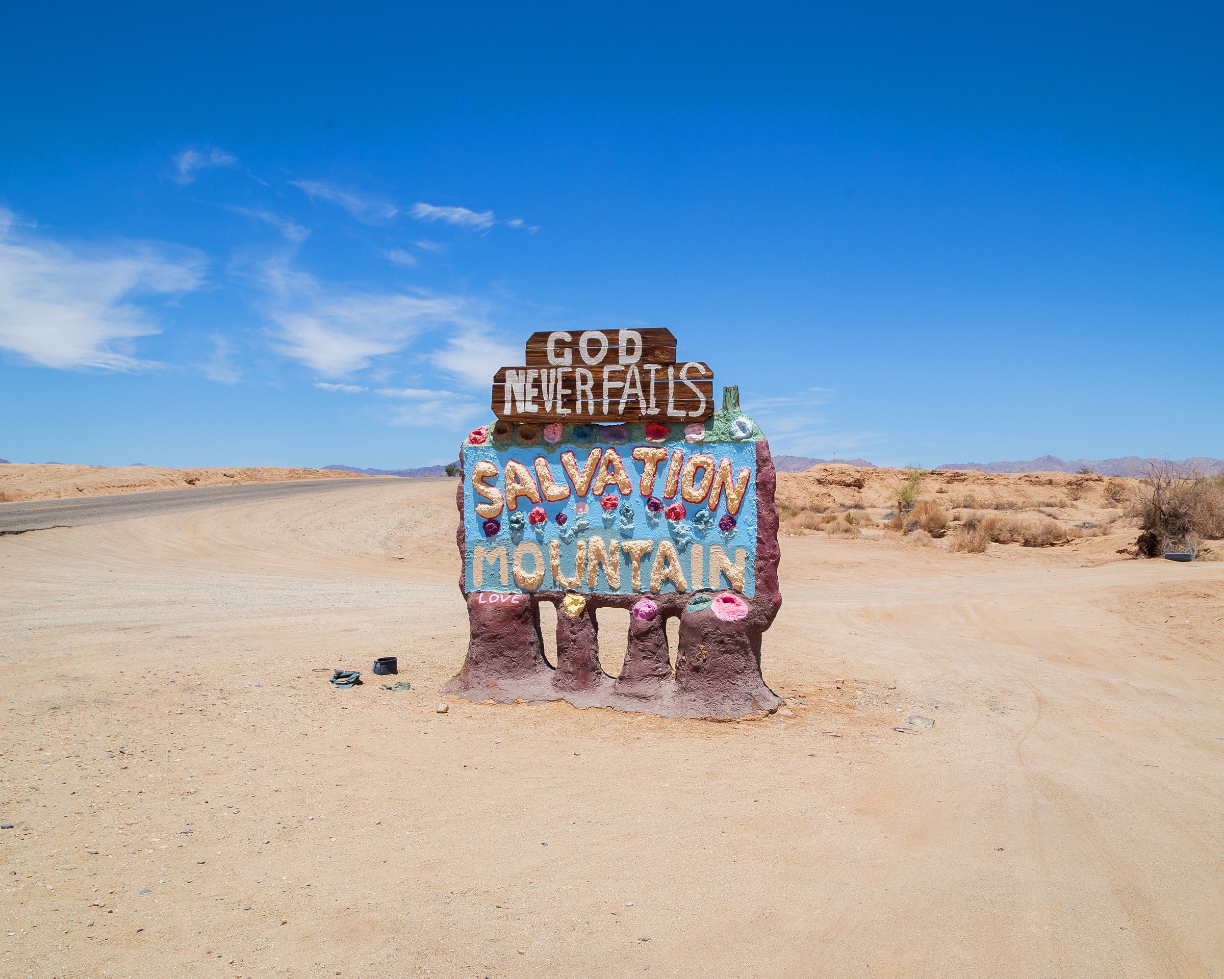 The Salvation Mountain sign on the dirt road in — God Never Fails, painted on a wooden offering